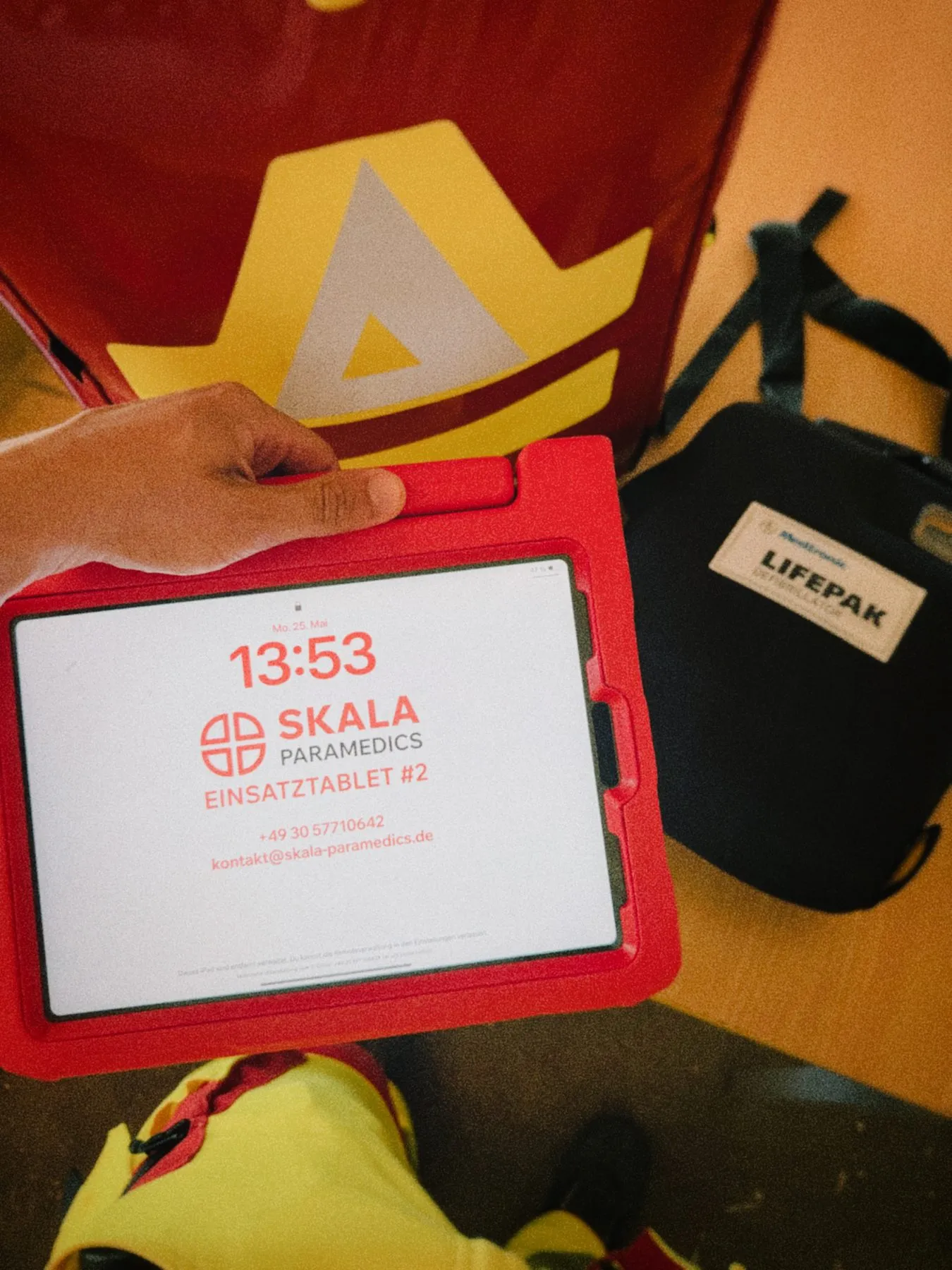 Einsatz-iPad mit SKALA-Logo vor Notfallrucksack und AED