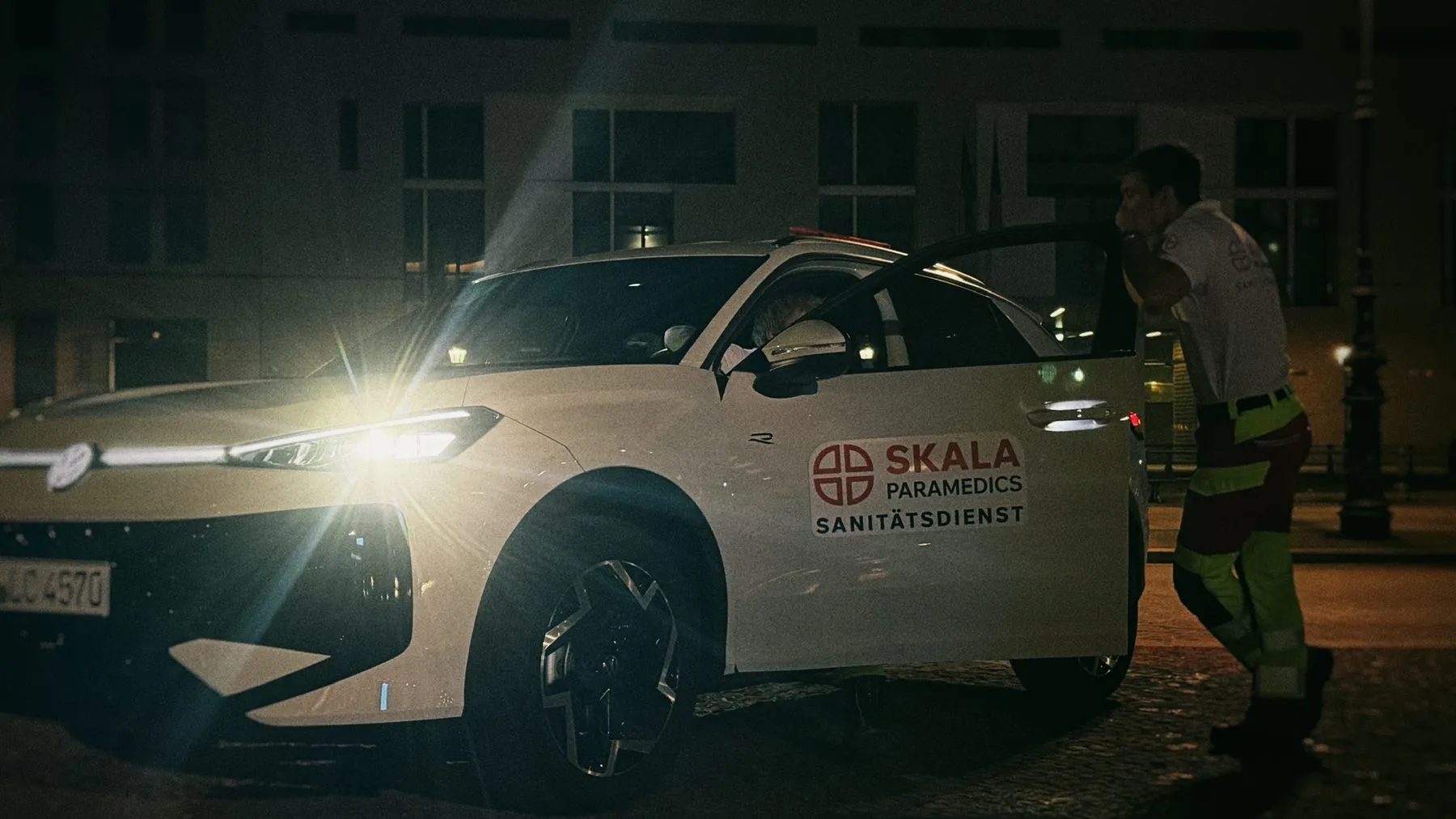 Weißes First-Responder-Fahrzeug von SKALA mit eingeschalteten Scheinwerfern bei Nacht