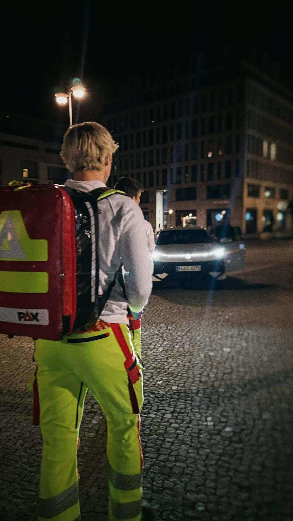 Sanitäter mit Notfallrucksack nachts an einer Straße, von hinten