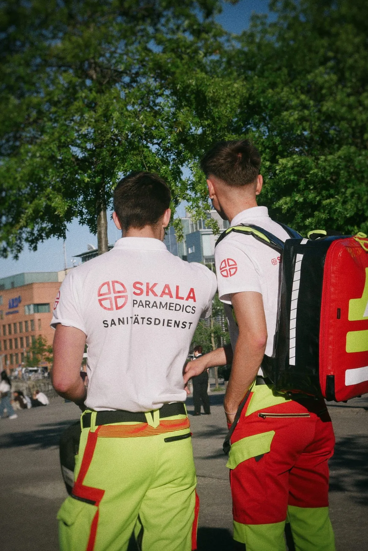 Zwei Sanitäter mit SKALA-Rückenaufdruck und Notfallrucksack unter Bäumen